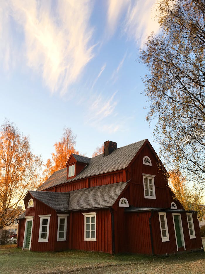 Picturesque red wooden house in autumn. Traditional Swedish architecture amidst colorful foliage.