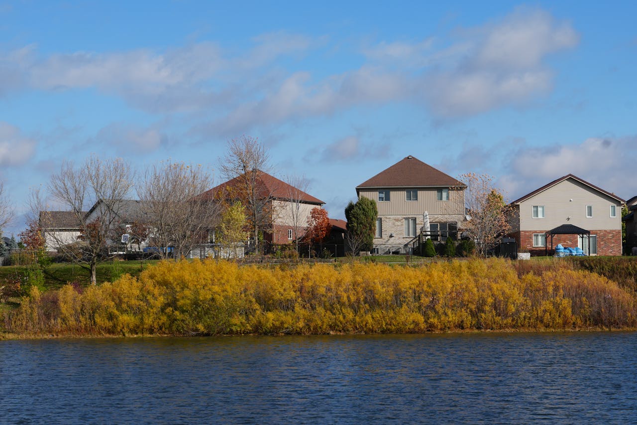 Peaceful view of suburban homes by a lake with autumn foliage.