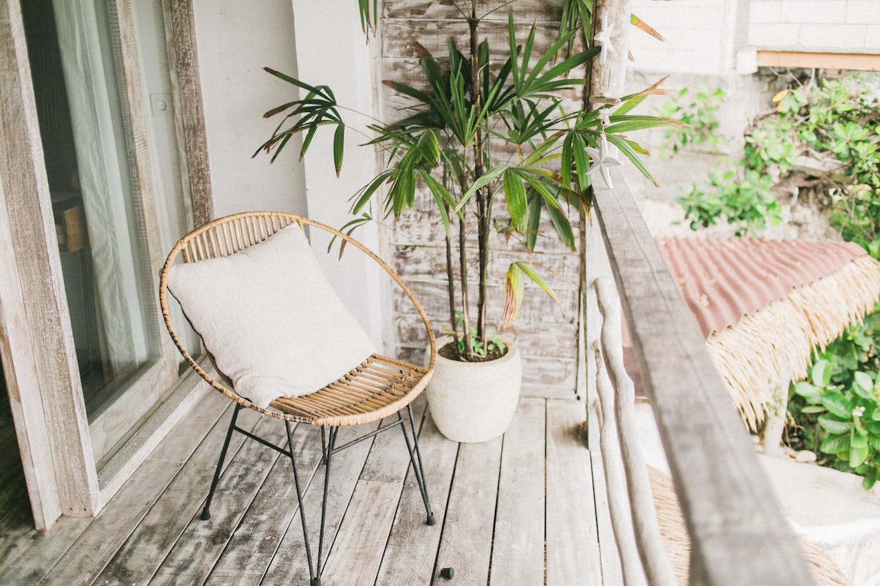 Tranquil outdoor balcony area featuring a rattan chair with a cushion and vibrant green potted plant.