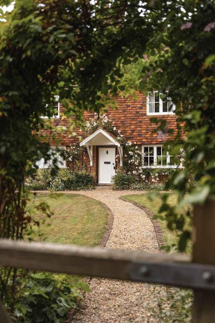 A rustic English cottage framed by lush greenery and a winding garden path, ideal for serene rural living.